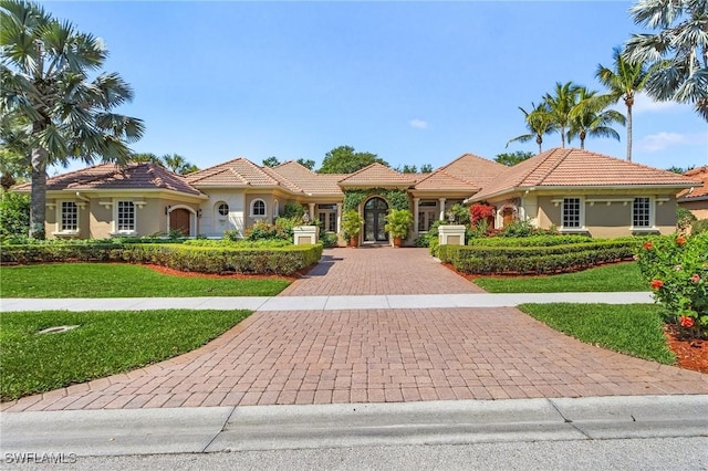 mediterranean / spanish home featuring a front yard, a tiled roof, decorative driveway, and stucco siding