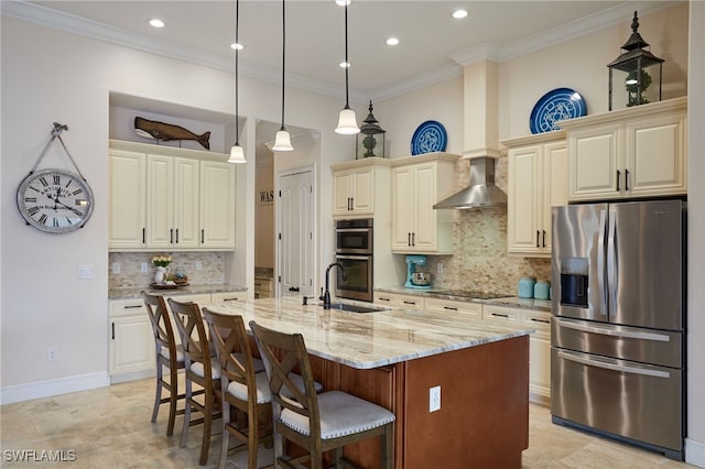kitchen with a sink, stainless steel appliances, light stone counters, wall chimney exhaust hood, and cream cabinetry