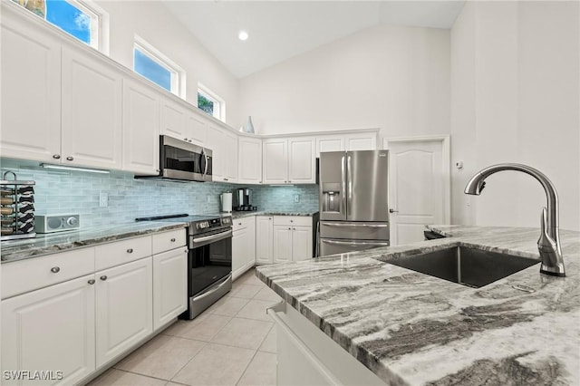 kitchen with appliances with stainless steel finishes, high vaulted ceiling, a sink, and light stone countertops