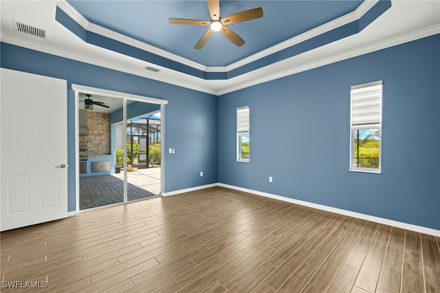 empty room with a tray ceiling, visible vents, baseboards, wood finished floors, and ceiling fan