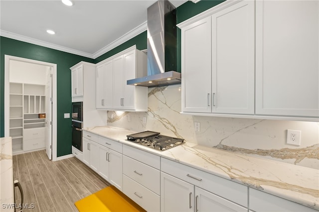 kitchen featuring wall chimney range hood, tasteful backsplash, black appliances, white cabinets, and ornamental molding