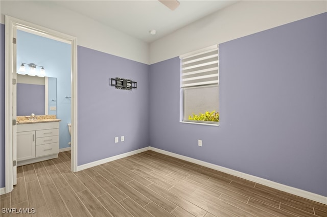 unfurnished bedroom with light wood-style floors, connected bathroom, baseboards, and a sink