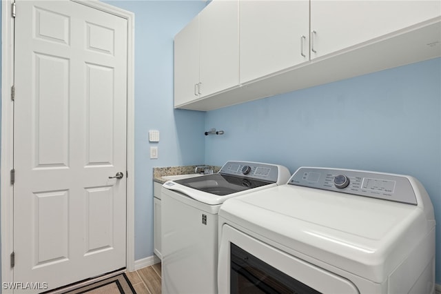 washroom featuring washing machine and dryer, a sink, light wood-type flooring, and cabinet space