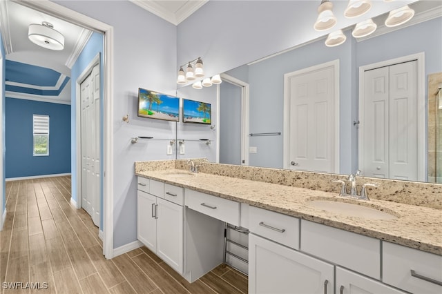 bathroom featuring wood finish floors, ornamental molding, a sink, and baseboards