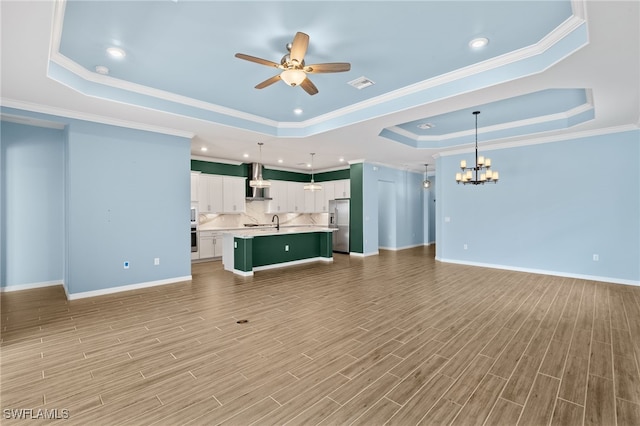 unfurnished living room featuring a tray ceiling, visible vents, light wood finished floors, and ceiling fan with notable chandelier