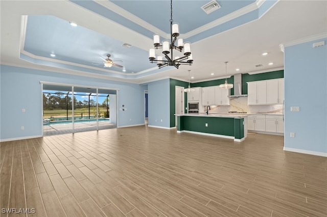 unfurnished living room featuring ceiling fan with notable chandelier, visible vents, a raised ceiling, and crown molding