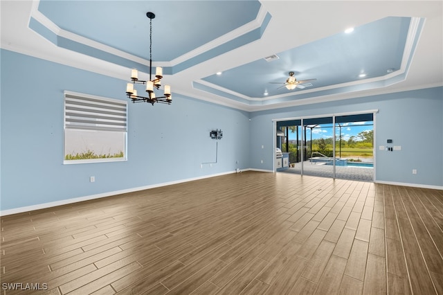empty room with a tray ceiling, dark wood-style floors, baseboards, ceiling fan with notable chandelier, and crown molding