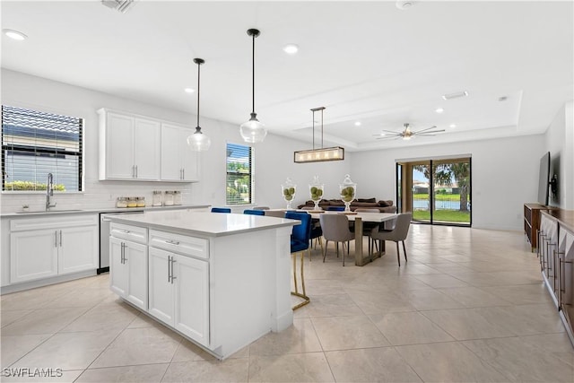 kitchen with a tray ceiling, a kitchen island, a sink, light countertops, and backsplash