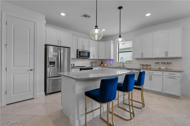 kitchen with light tile patterned floors, white cabinetry, a kitchen island, a sink, and stainless steel appliances