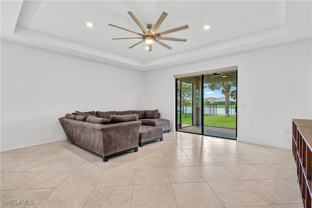 living room featuring a raised ceiling, ceiling fan, baseboards, and light tile patterned floors