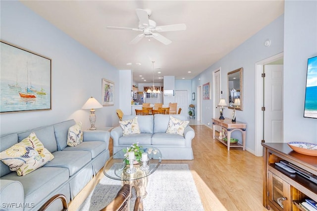 living area with light wood-style floors, ceiling fan with notable chandelier, and baseboards