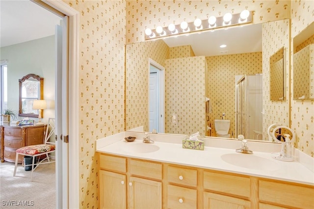 bathroom featuring a shower stall, double vanity, a sink, and wallpapered walls