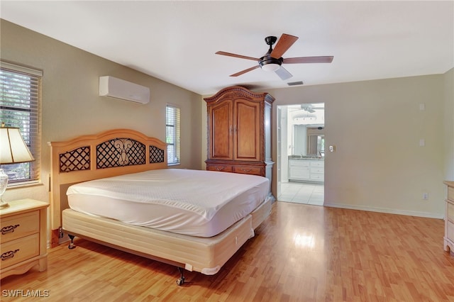 bedroom with a wall mounted air conditioner, ensuite bathroom, light wood finished floors, baseboards, and visible vents