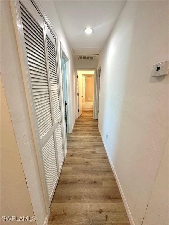 hallway with a heating unit, visible vents, light wood-style flooring, and baseboards