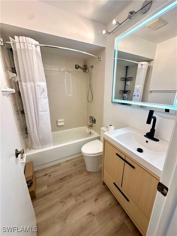 bathroom featuring wood finished floors, shower / bath combo with shower curtain, toilet, vanity, and visible vents