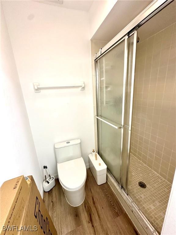 bathroom with wood finished floors, toilet, and a stall shower