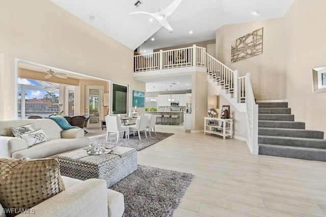 living room featuring a ceiling fan, a towering ceiling, stairs, light wood finished floors, and baseboards