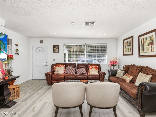 living area featuring visible vents, baseboards, light wood finished floors, and a textured ceiling