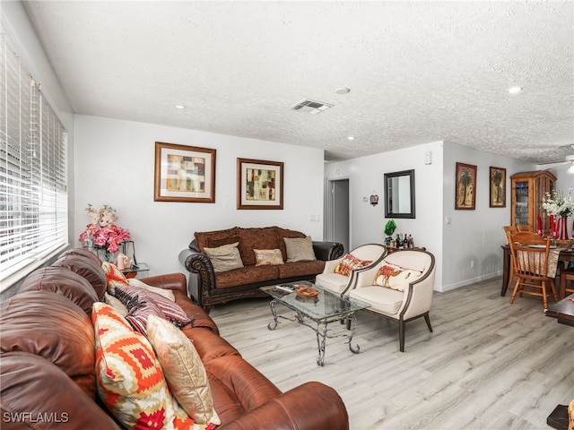 living area with visible vents, a textured ceiling, baseboards, and wood finished floors