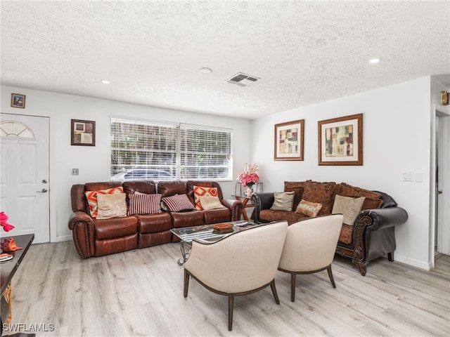 living area with light wood finished floors, visible vents, and a textured ceiling