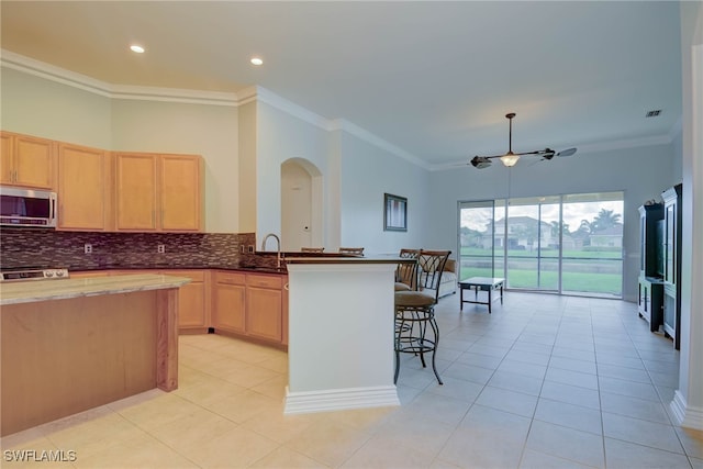 2042 Mandarin Ln, Naples, FL 34120 - kitchen with stainless steel microwave, light brown cabinetry, tasteful backsplash, ornamental molding, and a kitchen breakfast bar
