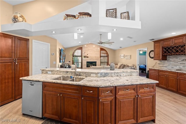 kitchen featuring light wood-style floors, vaulted ceiling, dishwasher, a sink, and a premium fireplace