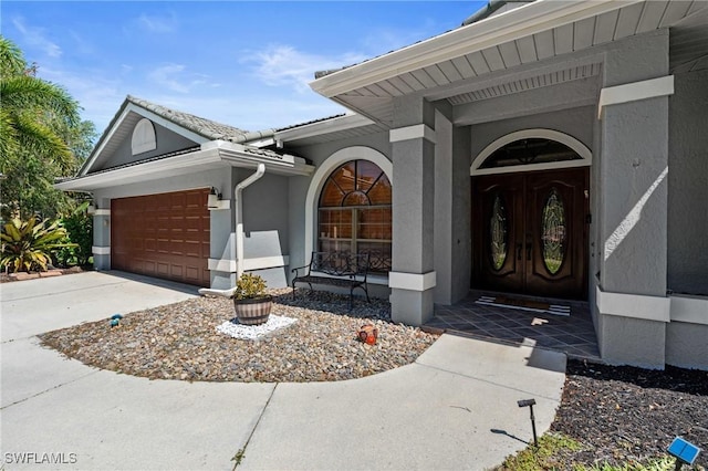 doorway to property with an attached garage, concrete driveway, and stucco siding