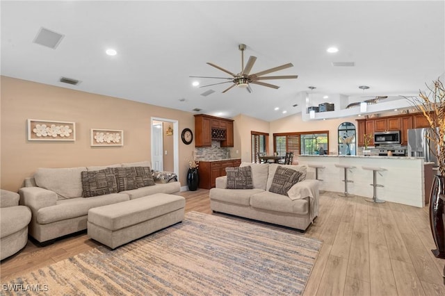 living room with visible vents, light wood-type flooring, vaulted ceiling, and a ceiling fan