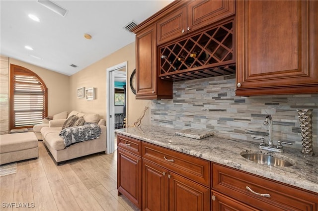 bar featuring visible vents, indoor wet bar, a sink, light wood finished floors, and lofted ceiling