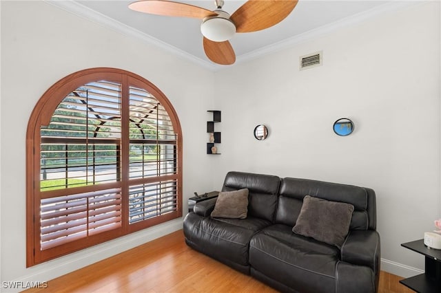 living room featuring baseboards, ornamental molding, visible vents, ceiling fan, and wood finished floors