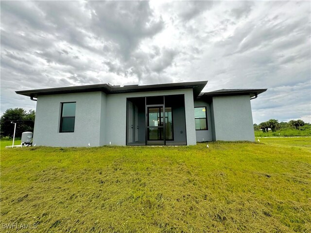 rear view of house featuring stucco siding and a lawn