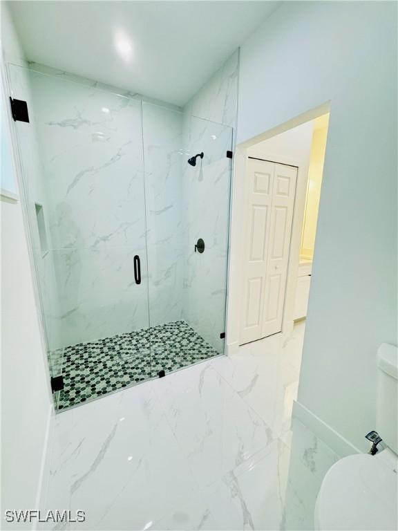 bathroom with toilet, marble finish floor, baseboards, and a marble finish shower