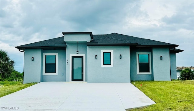 view of front of home featuring a patio area, a front lawn, stucco siding, and roof with shingles
