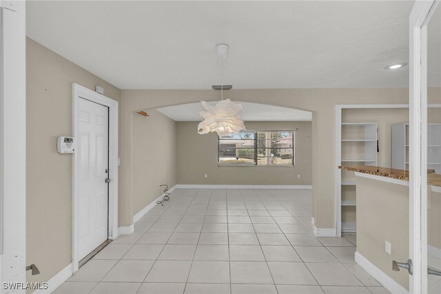 unfurnished dining area featuring an inviting chandelier, arched walkways, visible vents, light tile patterned flooring, and baseboards