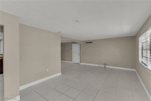 empty room featuring baseboards, arched walkways, and light tile patterned flooring