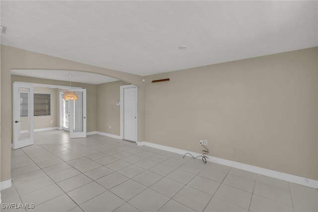 spare room with arched walkways, light tile patterned floors, and baseboards