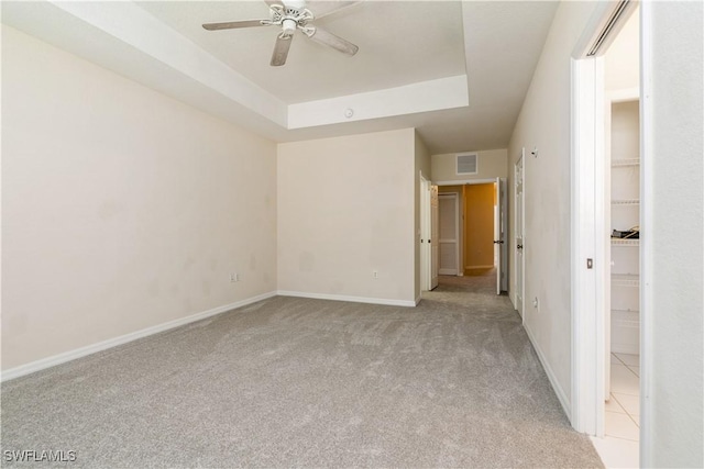 unfurnished bedroom with a tray ceiling, light carpet, a spacious closet, and visible vents