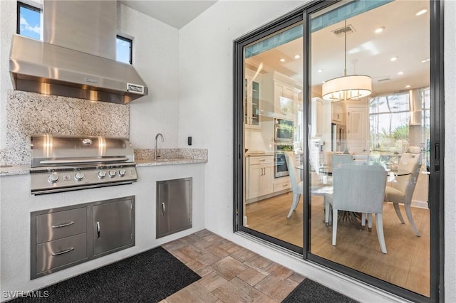 interior space featuring a healthy amount of sunlight, wall chimney range hood, backsplash, and stainless steel oven