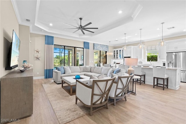 living room featuring a wealth of natural light, light wood-style flooring, a tray ceiling, and crown molding