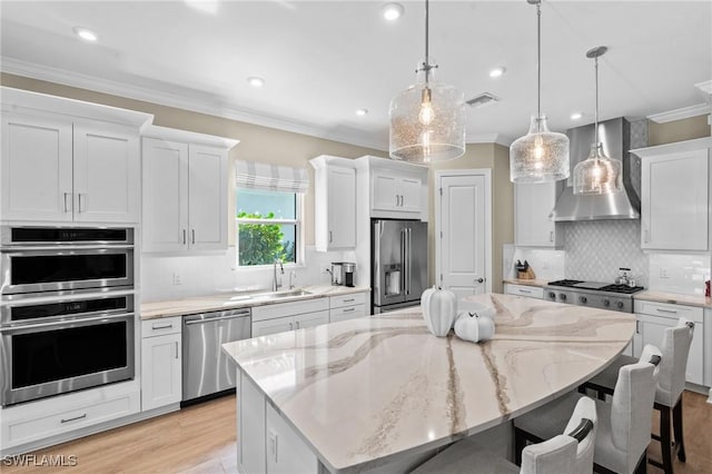 kitchen featuring crown molding, wall chimney exhaust hood, a breakfast bar area, appliances with stainless steel finishes, and a sink