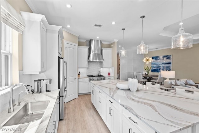 kitchen with a large island, ornamental molding, wall chimney range hood, visible vents, and a sink