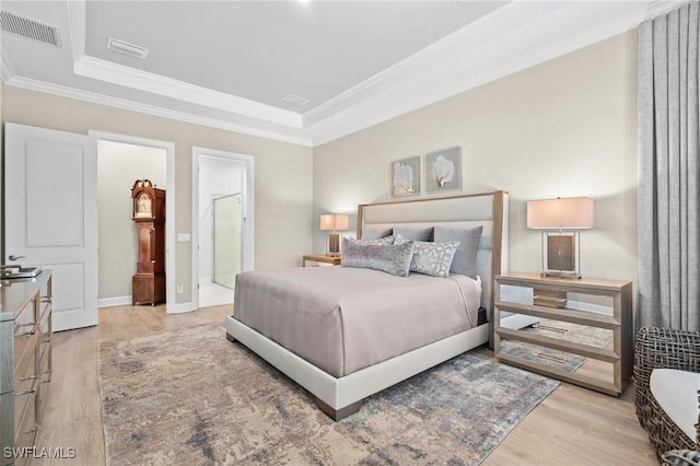 bedroom featuring ornamental molding, visible vents, light wood-style flooring, and a tray ceiling