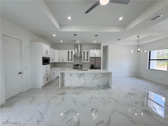 kitchen with visible vents, wall chimney range hood, a tray ceiling, ceiling fan with notable chandelier, and stainless steel appliances