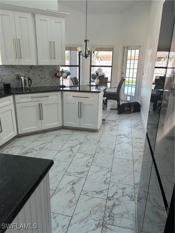 8860 Banyan Cove Cir S Unit 0, Fort Myers, FL 33919 - kitchen featuring light marble finish floors, a chandelier, dark countertops, and tasteful backsplash