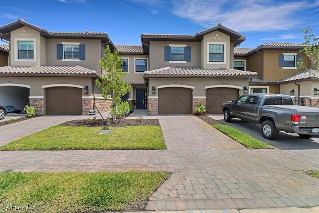 townhome / multi-family property with stucco siding, a tile roof, and stone siding