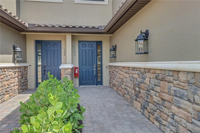 view of exterior entry featuring stone siding and stucco siding