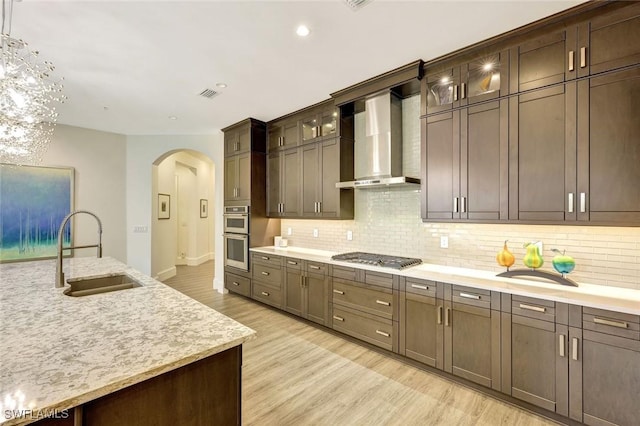 16358 Corsica Way Unit 201, Naples, FL 34110 - kitchen with wall chimney range hood, a sink, arched walkways, stainless steel gas cooktop, and light wood-style floors