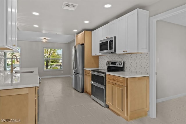 kitchen featuring appliances with stainless steel finishes, a sink, light countertops, baseboards, and decorative backsplash