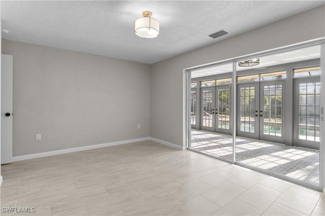 unfurnished room featuring french doors, a textured ceiling, baseboards, and visible vents