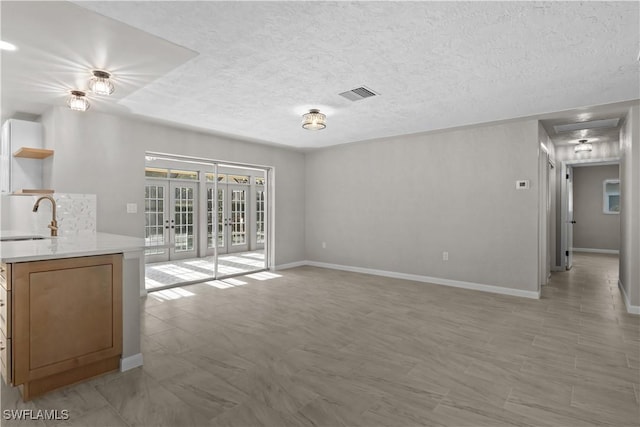 unfurnished living room with visible vents, baseboards, a textured ceiling, french doors, and a sink